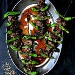 Four Grilled Japanese Beef and Shishito Pepper Skewers on oval gray-rimmed platter garnished with sesame seeds.