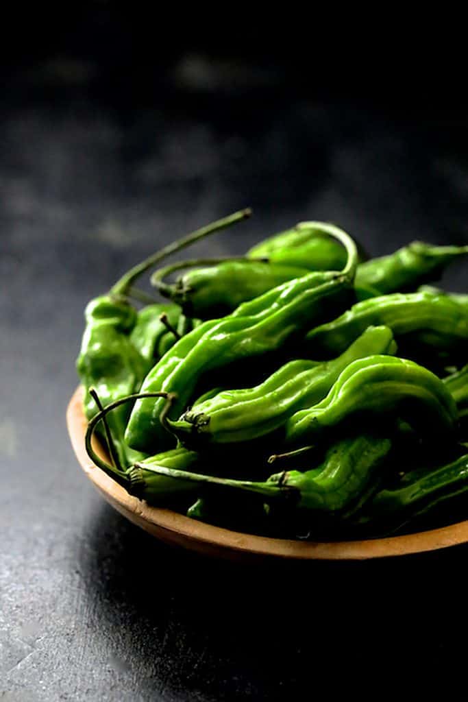 Photo of fresh, uncooked peppers in wooden bowl on dark gray background.