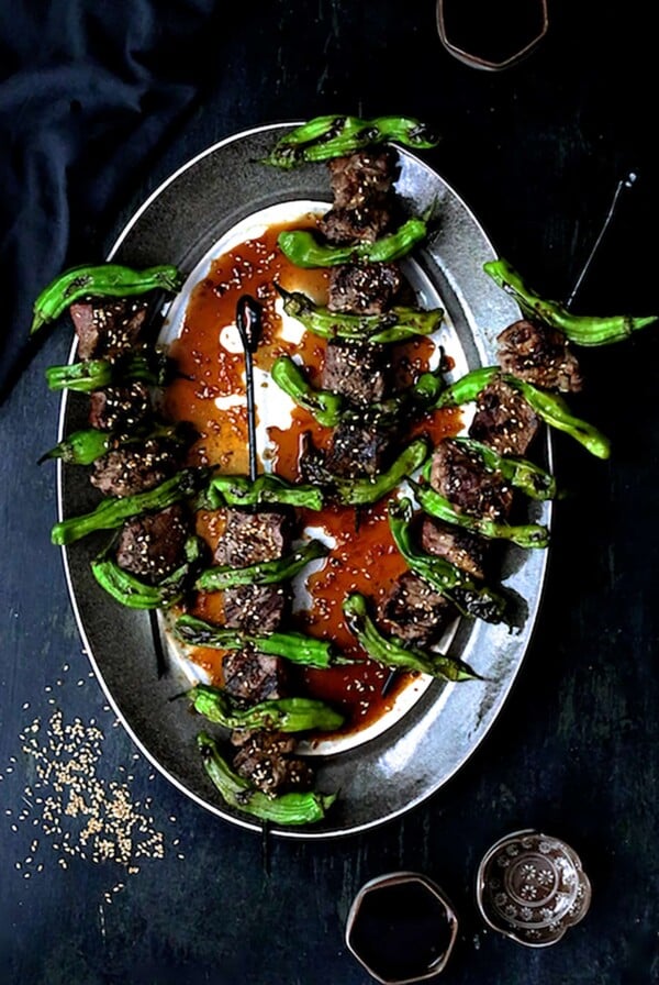 Four Grilled Japanese Beef and Shishito Pepper Skewers on oval gray-rimmed platter garnished with sesame seeds.