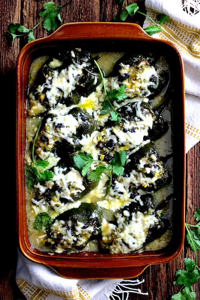 Photo of Quinoa Corn and Black Bean Stuffed Poblano Peppers in terra cotta baking dish on wood background garnished with cilantro.