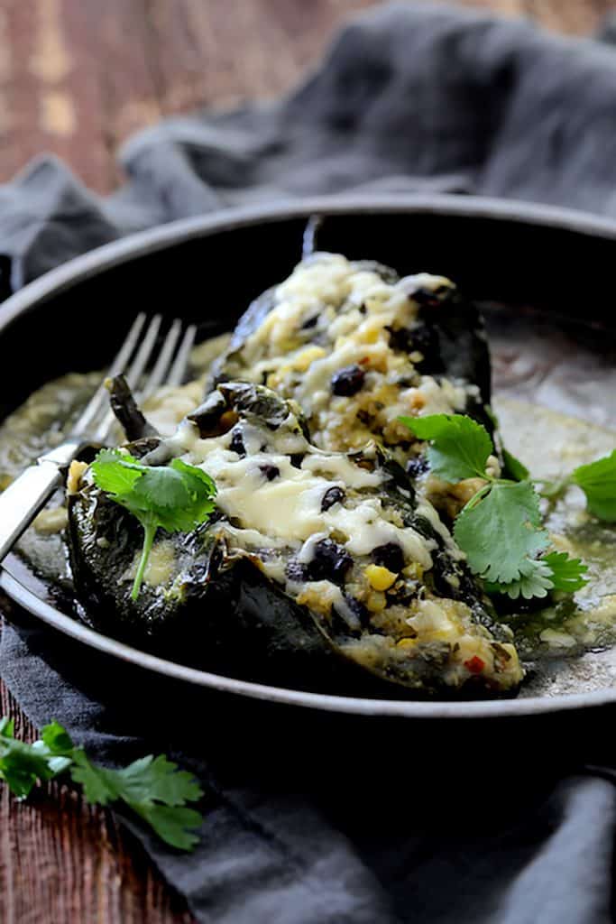 Close-up photo of one serving of Quinoa Corn and Black Bean Stuffed Poblano Peppers in dish on gray napkin garnished with cilantro.