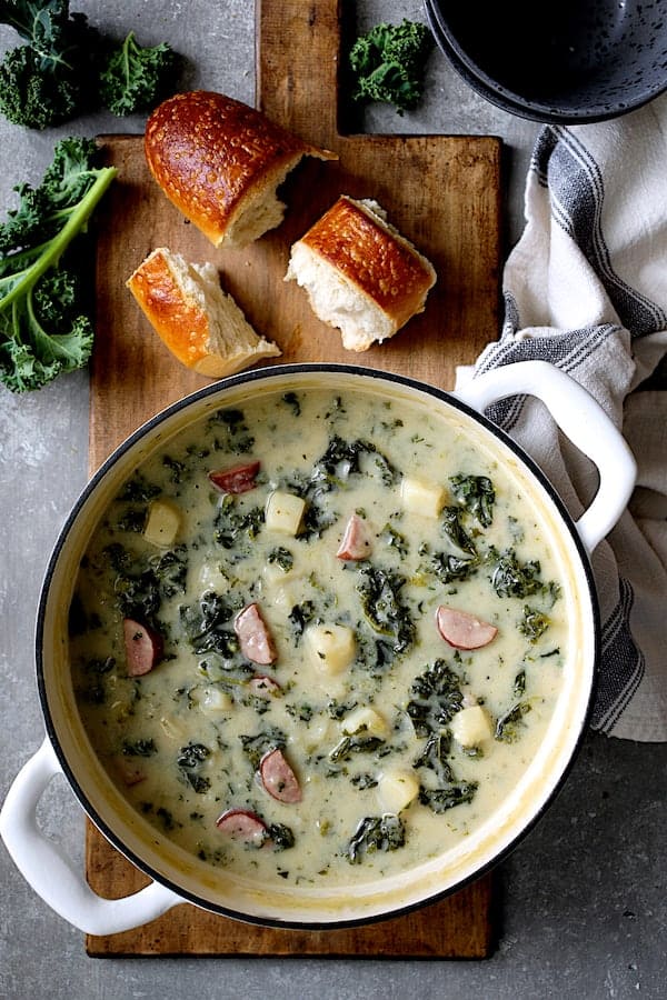 Photo of Creamy Potato Kielbasa and Kale Soup in white Dutch oven with bread and fresh kale.