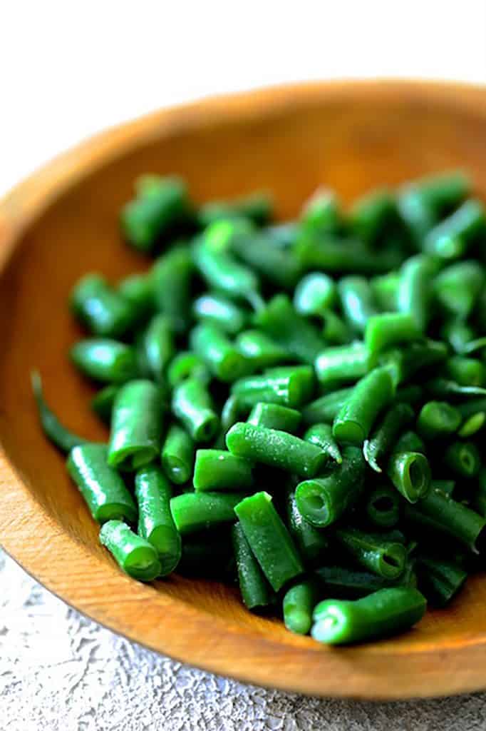 Photo of cooked green beans in wooden bowl.