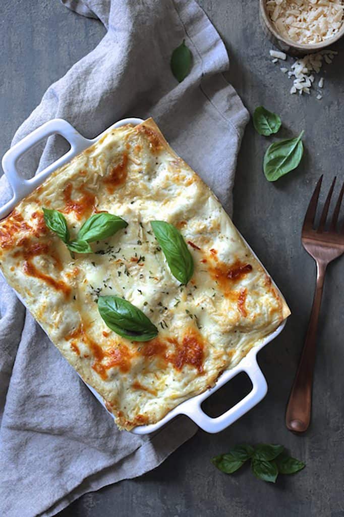 Photo of Lasagna with Pesto Green Beans and Potatoes garnished with fresh basil on gray background with serving fork.