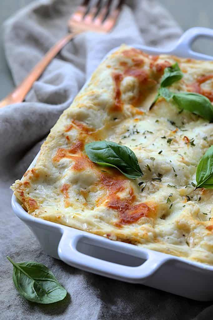 Photo of Lasagna with Pesto Green Beans and Potatoes in white baking dish garnished with fresh basil.