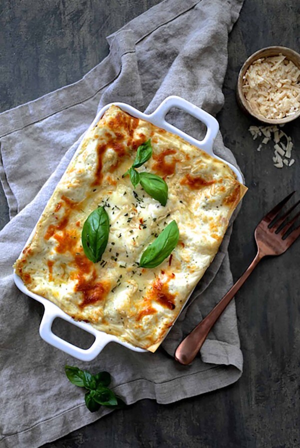 Lasagna with Pesto Green Beans and Potatoes in white baking dish on gray napkin.