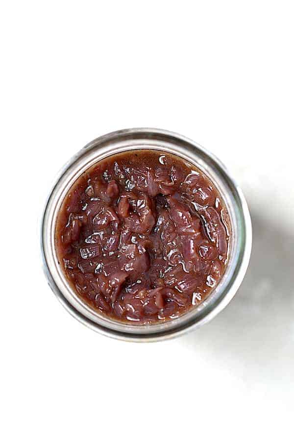 Photo of red onion marmalade in glass jar on white background.