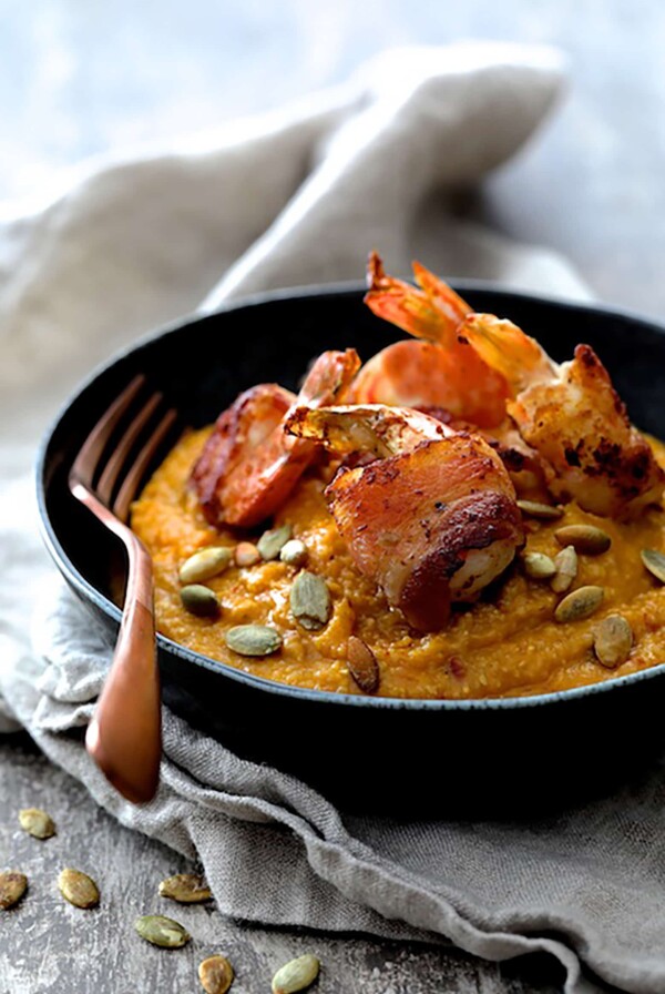 Pumpkin Chipotle and White Cheddar Grits with Bacon Wrapped Shrimp in black bowl garnished with pumpkin seeds.