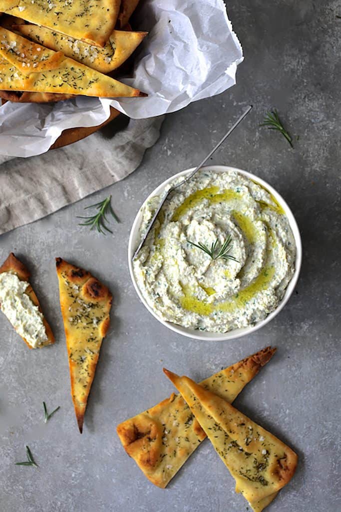 Photo of White Bean Artichoke Spread with Rosemary Sea Salt Flatbread Chips garnished with rosemary sprigs.