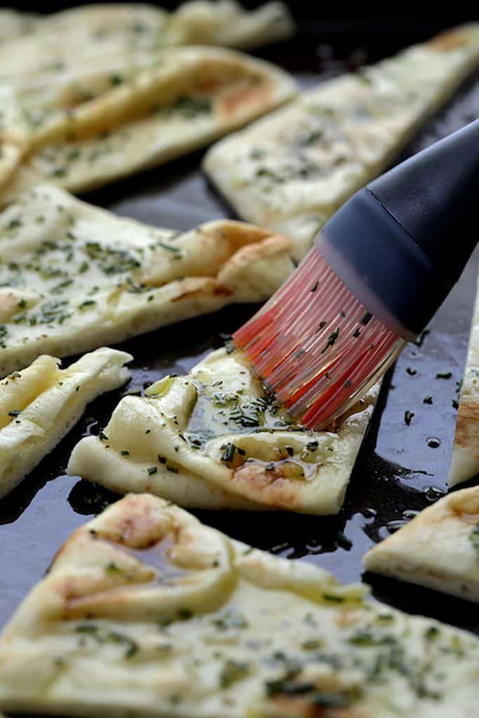 Photo of flatbread chips being brushed with olive oil and rosemary.