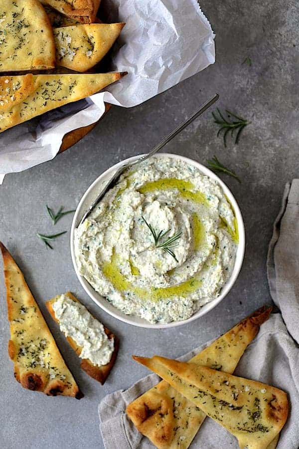 Photo of White Bean and Artichoke Spread with Rosemary Sea Salt Flatbread Chips on gray background garnished with fresh rosemary.