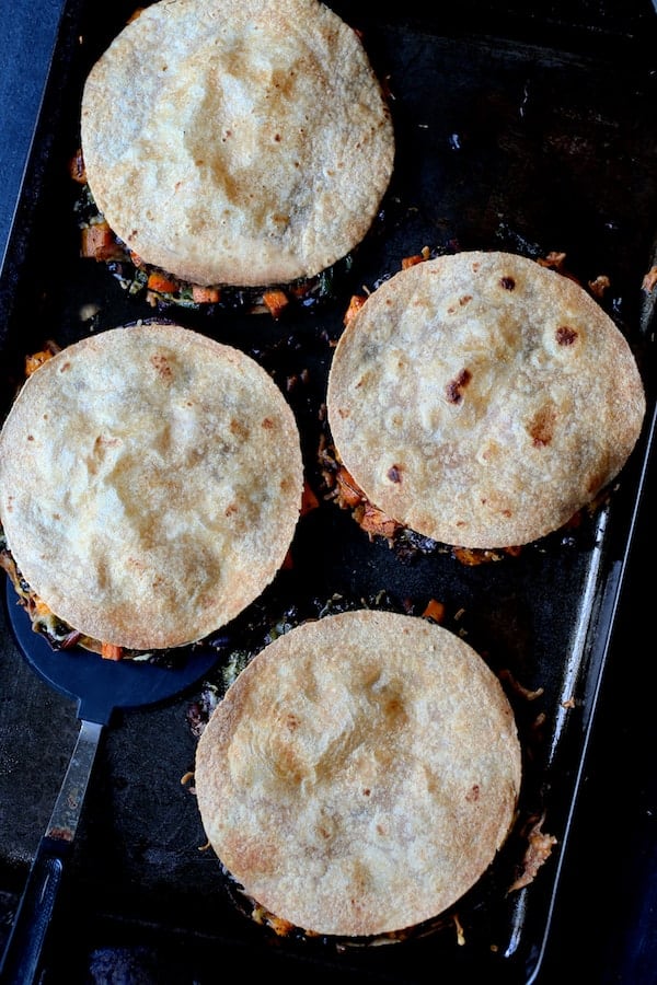 Photo of four assembled and baked Sheet Pan Quesadillas with Sweet Potatoes, Poblanos and Black Beans with Chipotle Sour Cream on baking sheet.