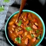 Slow Cooker Cajun 15 Bean Soup with Andouille Ham and Bacon in bright blue bowl with copper soup spoon.