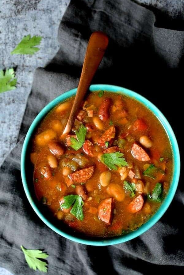 Slow Cooker Cajun 15 Bean Soup with Andouille Ham and Bacon in bright blue bowl with copper soup spoon.