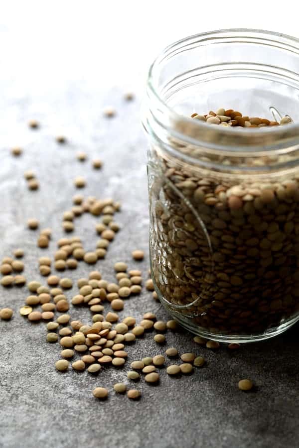 Photo of a jar of brown lentils with some scattered on surface.
