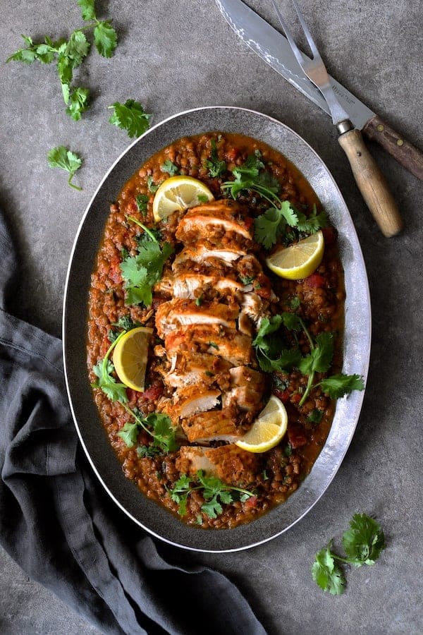 Photo of Slow Cooker Moroccan Turkey and Lentils on gray-rimmed platter garnished with cilantro and lemon wedges with gray napkin.