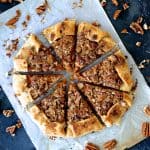 Sweet Potato Galette with Pecan Streusel Topping on white parchment paper cut into wedges with pecan pieces scattered around.