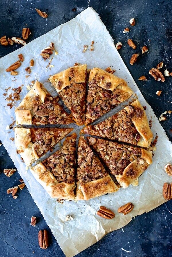 Sweet Potato Galette with Pecan Streusel Topping on white parchment paper cut into wedges with pecan pieces scattered around.