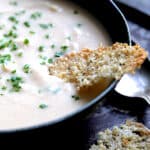 Creamy White Bean, Rutabaga and Roasted Garlic Soup with Quinoa Parmesan Crisps - Close-up shot of soup in black bowl garnished with fresh chives