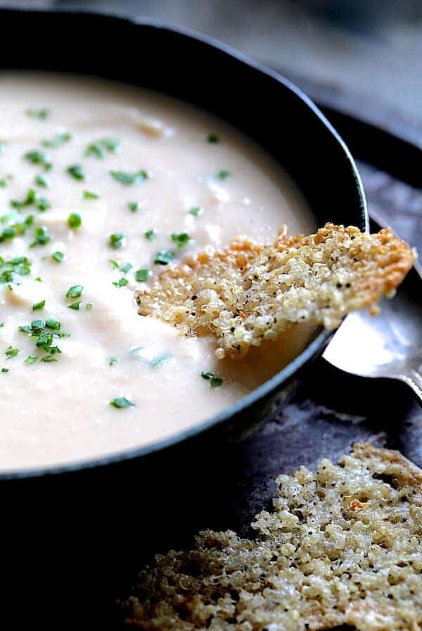 Creamy White Bean, Rutabaga and Roasted Garlic Soup with Quinoa Parmesan Crisps - Close-up shot of soup in black bowl garnished with fresh chives