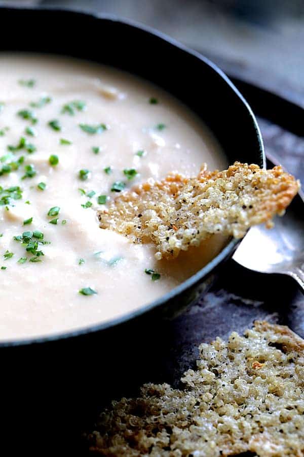 Close-up photo of Creamy White Bean, Rutabaga and Roasted Garlic Soup in black bowl garnished with fresh chives.