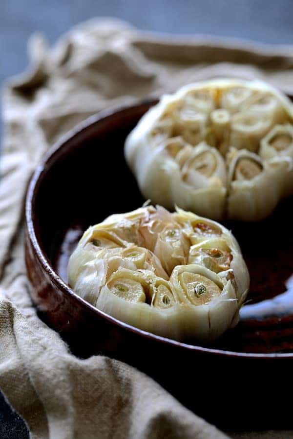 Photo of roasted garlic in terra cotta baking dish.