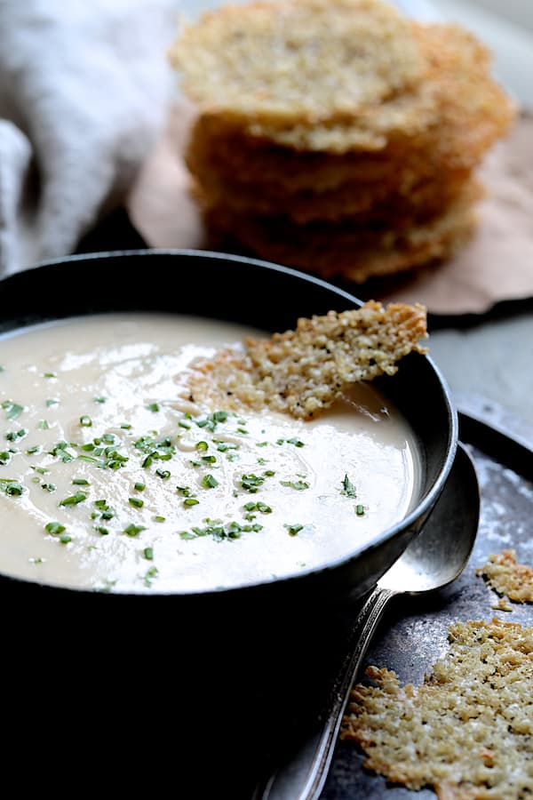 Photo of Creamy White Bean Rutabaga and Roasted Garlic Soup in black bowl with Quinoa Parmesan Crisps.