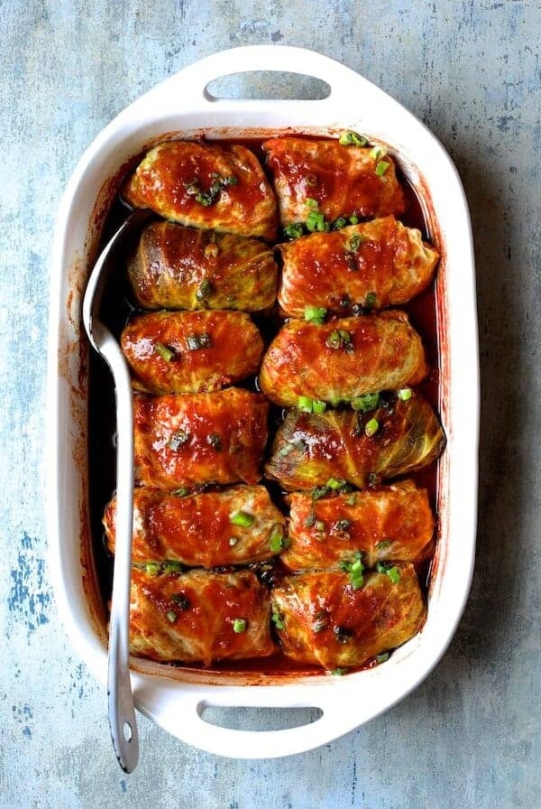 Spicy Asian Pork Cabbage Rolls in white baking dish with white serving spoon after being baked.