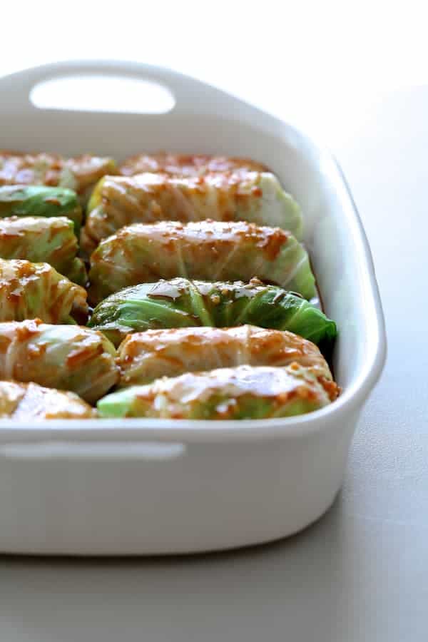 Photo of uncooked cabbage rolls in white baking pan with sauce drizzled over the top.