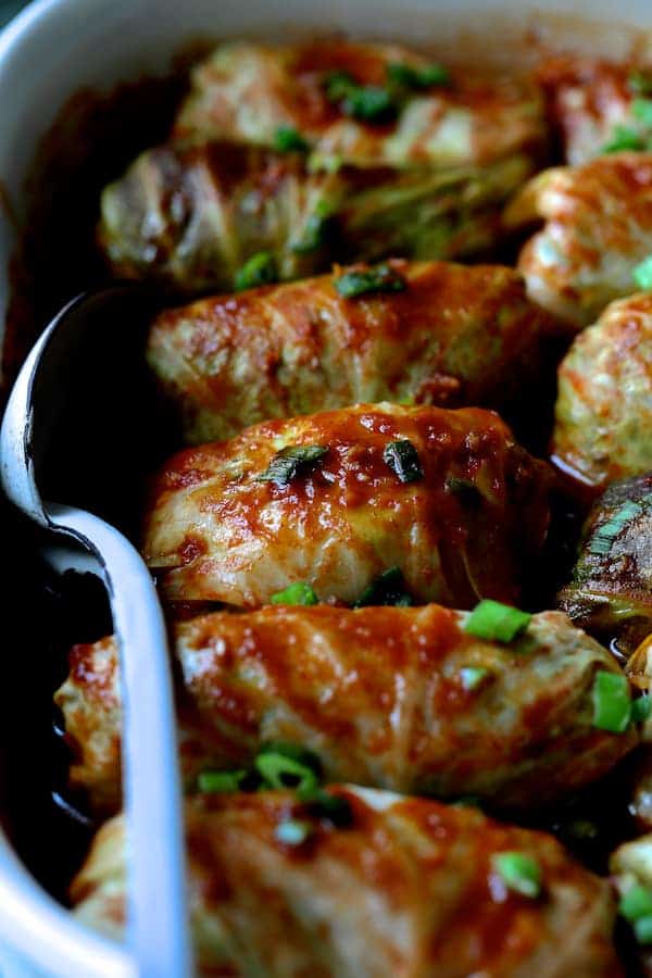 Close-up photo of Spicy Asian Pork Cabbage Rolls in white baking dish with white metal spoon.