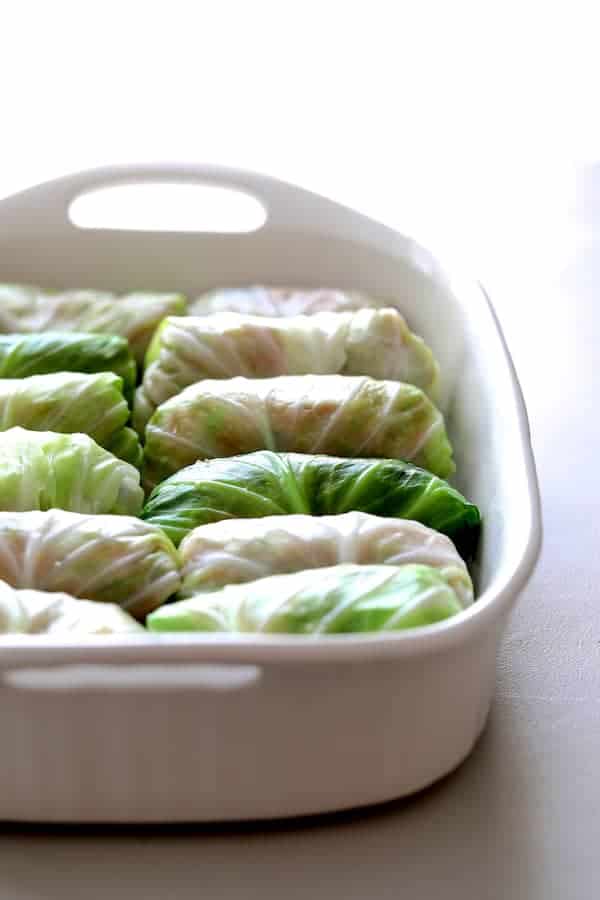 Photo of uncooked cabbage rolls in white baking dish.