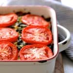 Brown Rice, Cheddar and Kale Casserole on white background with striped towel on wood trivet after baking.