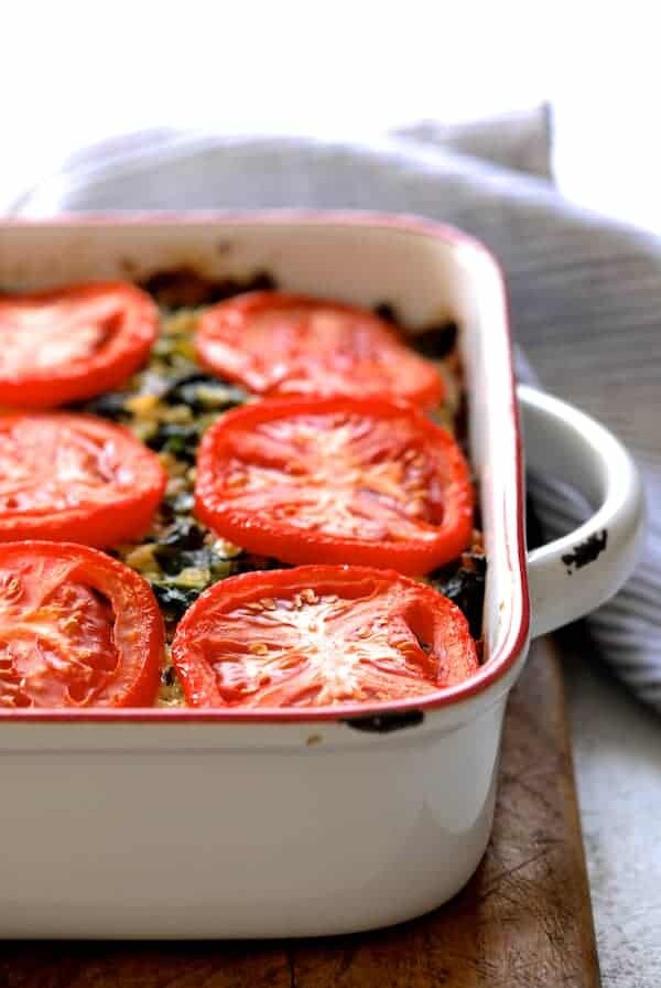 Brown Rice, Cheddar and Kale Casserole on white background with striped towel on wood trivet after baking.