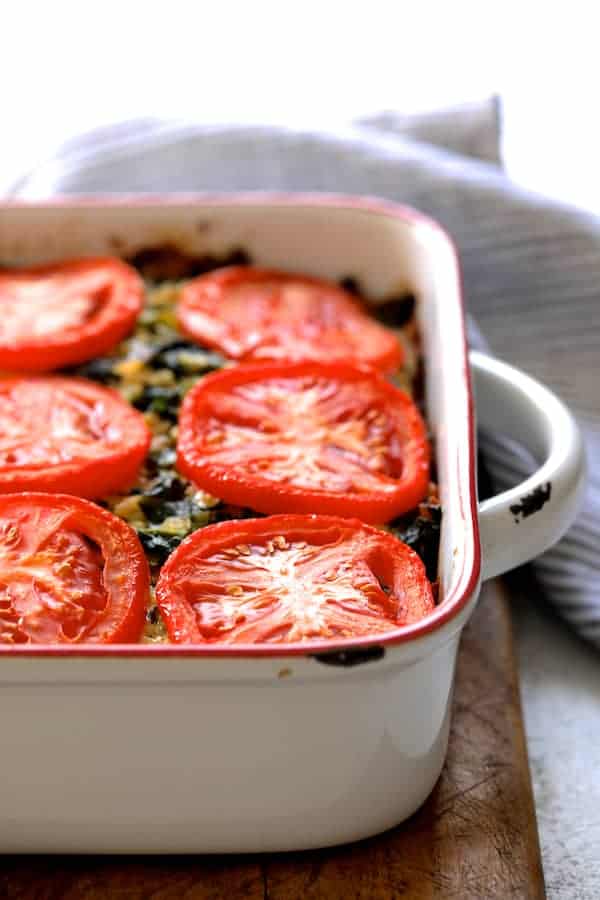 Photo of Brown Rice, Cheddar Kale Casserole on white background with striped towel on wood trivet after being baked.