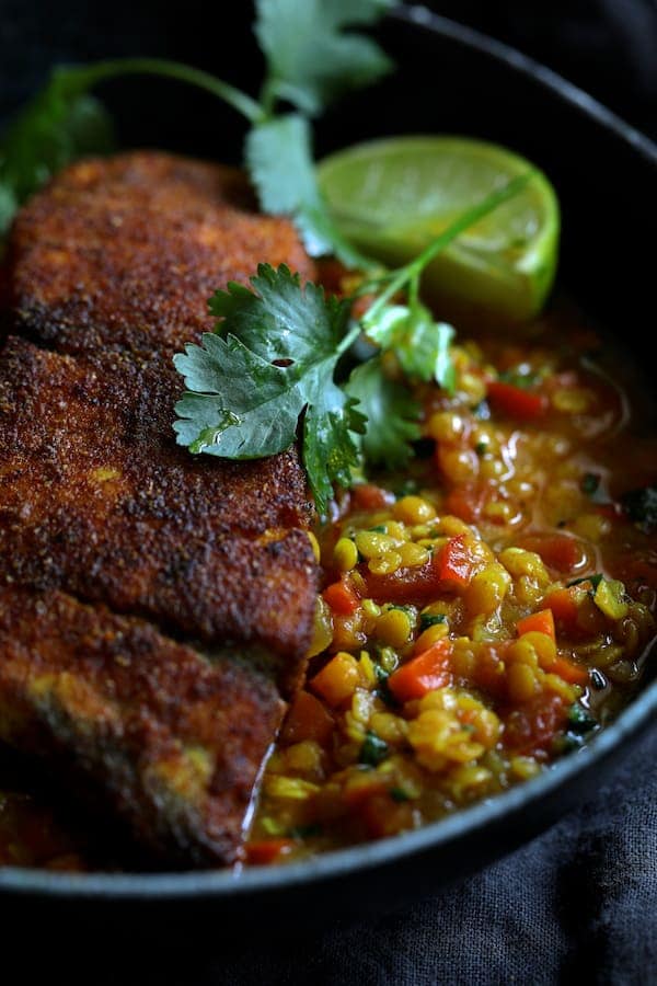 Close-up photo of one serving of Indian Spiced Sea Bass with Braised Red Lentils with cilantro sprig and lime wedge.