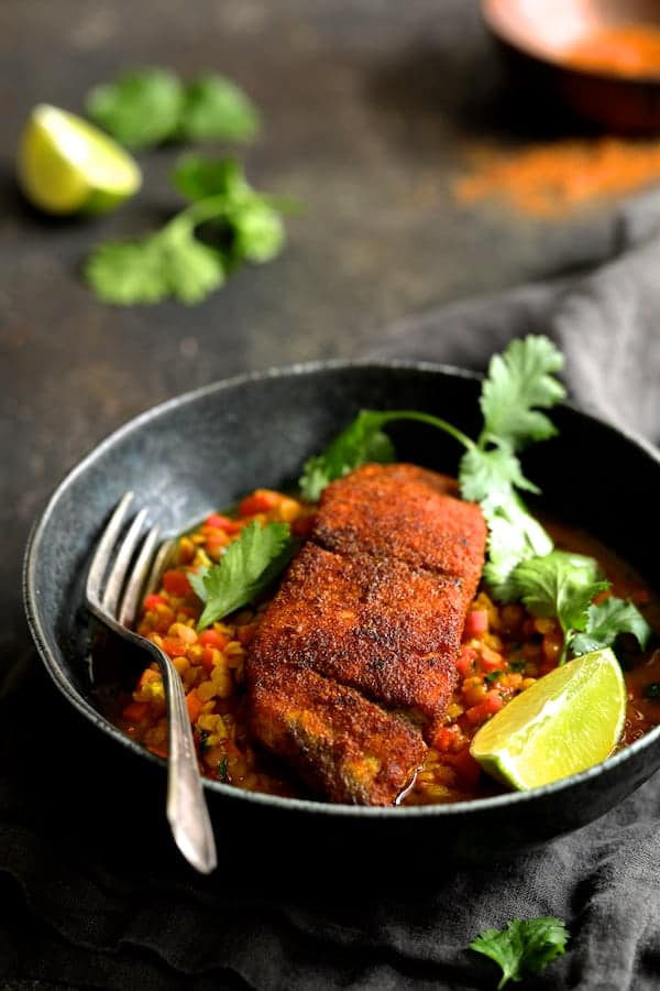 Photo of Indian Spiced Sea Bass with Braised Red Lentils in bowl with fork, cilantro sprigs and lime wedges.