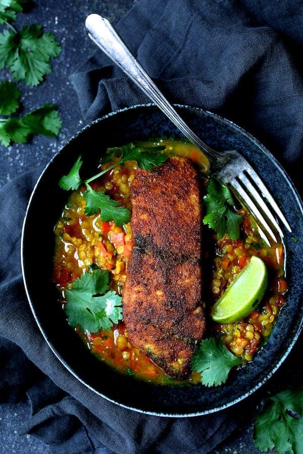 Photo of one serving of Indian Spiced Sea Bass with Braised Red Lentils in bowl with cilantro sprigs and lime wedges.