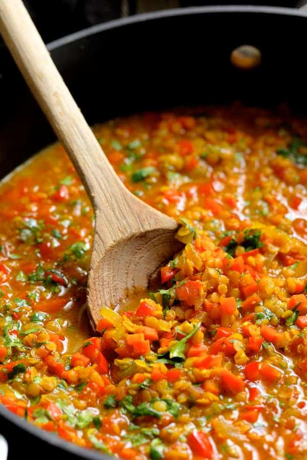 Photo of red lentils cooking being cooked and stirred in pot.