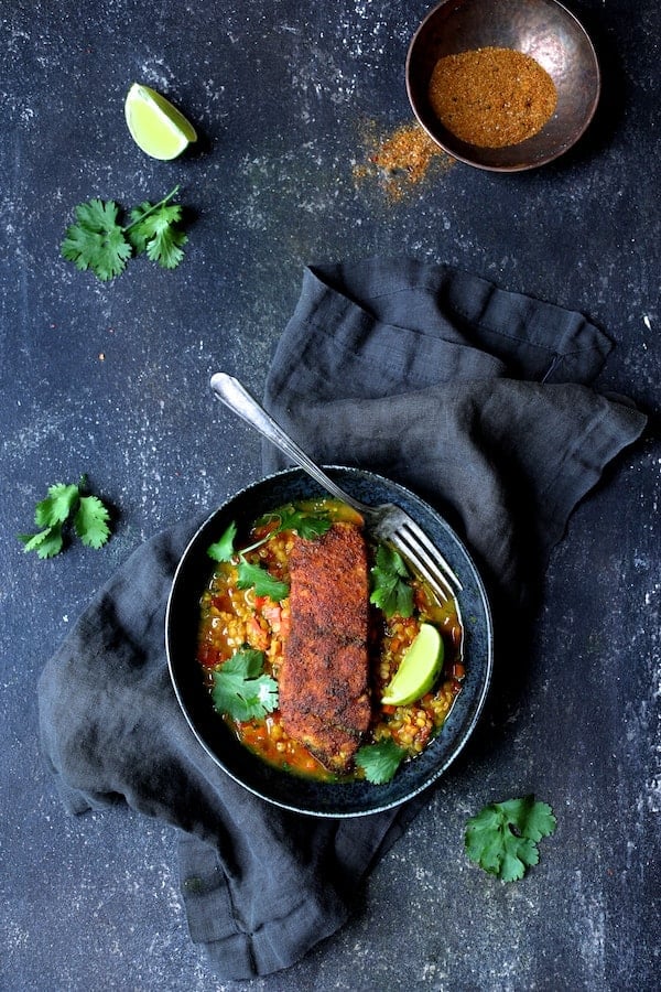 Photo of Indian Spiced Sea Bass with Braised Red Lentils on blue background with deep blue napkin garnished with cilantro sprigs.