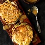 Two Roasted Cabbage Steaks with Mustard Vinaigrette on wood cutting board with sauce drizzled over.