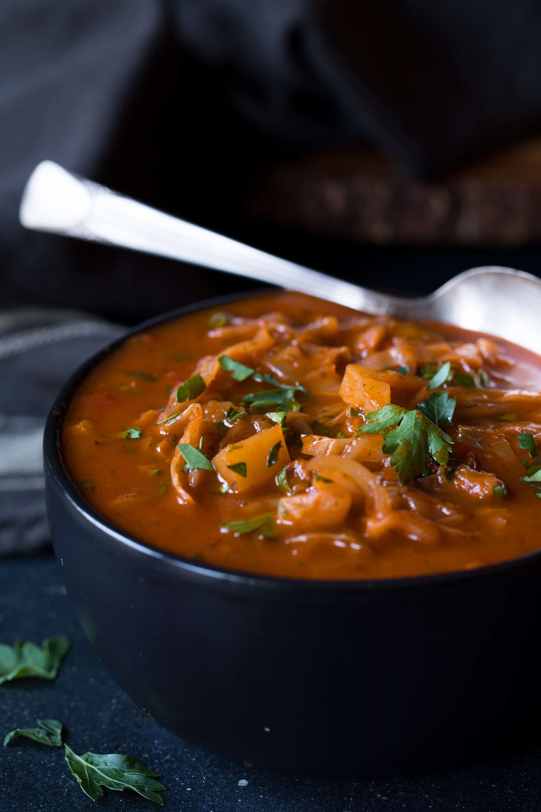 Close-up photo of Rustic Cabbage and Root Vegetable Soup in black bowl with spoon.