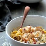 Seared Sea Scallops with Spicy Bacon Sun Dried Tomato Alfredo Sauce in white bowl with pasta twirled around a copper fork.