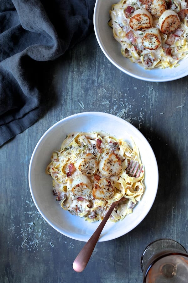 Photo of Seared Sea Scallops with Spicy Bacon and Sun Dried Tomato Alfredo Sauce on gray background with gray napkin.