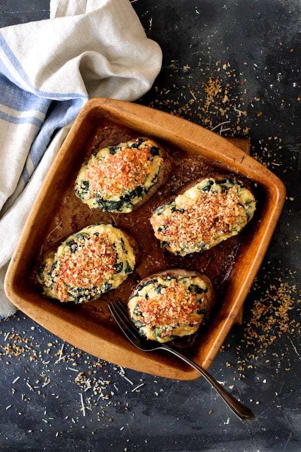 Photo of Spinach Parmesan Ranch Twice Baked Potatoes in clay baking dish with blue striped towel.