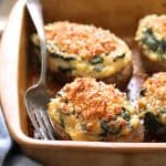 Spinach Parmesan Ranch Twice Baked Potatoes close up shot in clay baking dish with serving fork and blue striped towel.