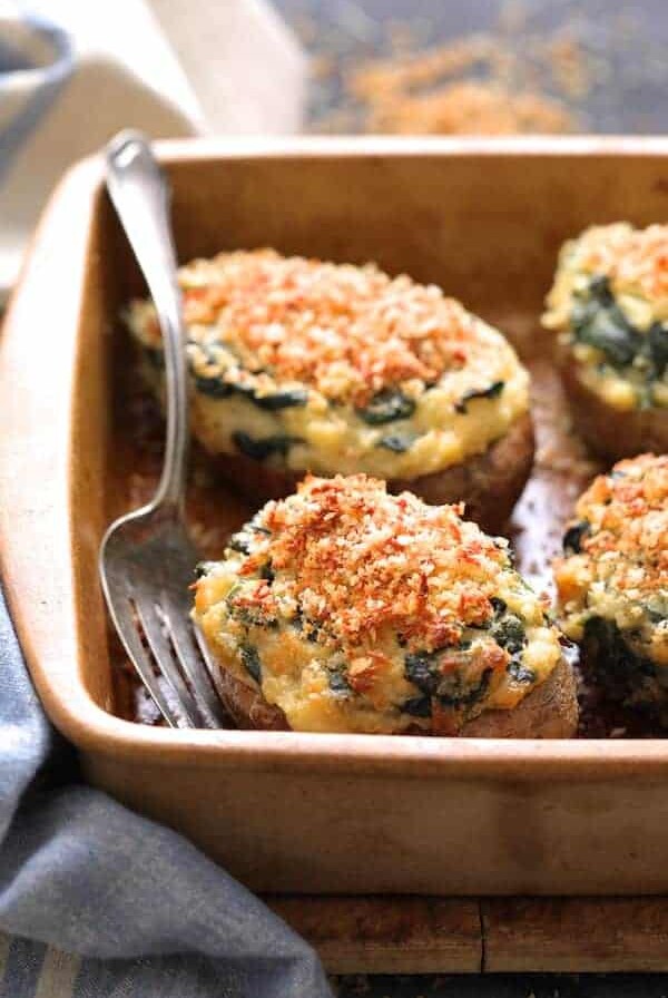 Spinach Parmesan Ranch Twice Baked Potatoes close up shot in clay baking dish with serving fork and blue striped towel.