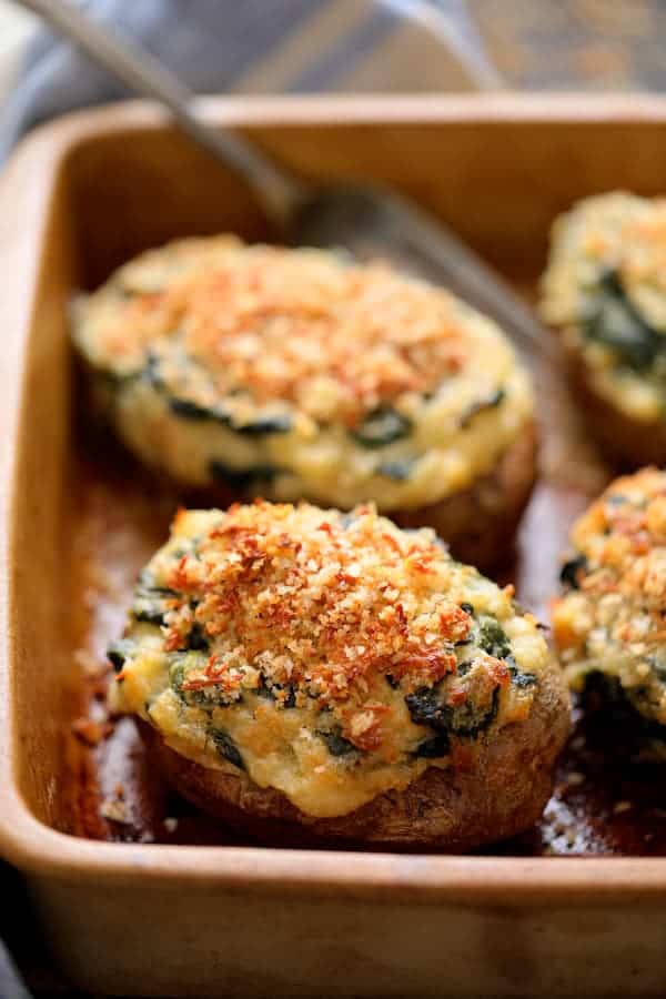 Close-up photo of Spinach Parmesan Ranch Twice Baked Potatoes in clay baking dish with serving fork.