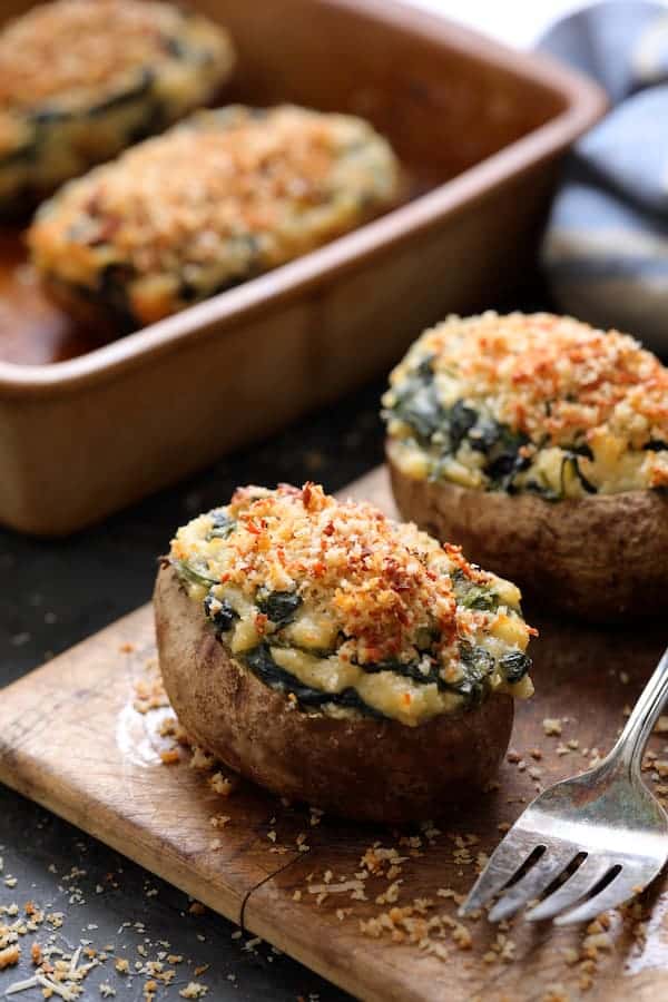 Photo of Spinach Parmesan Ranch Twice Baked Potatoes on small wooden cutting board with serving fork.