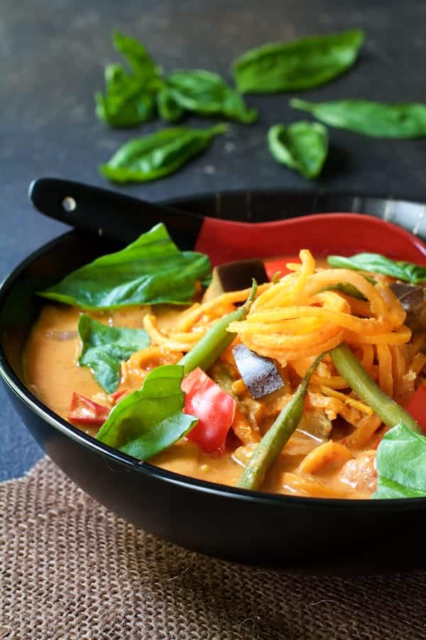 Photo of Vegetables in Thai Red Curry with Sweet Potato Noodles in black bowl on brown burlap.