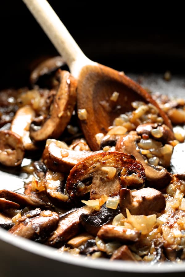 Photo of mushrooms being sauteed in pan with wooden spoon.